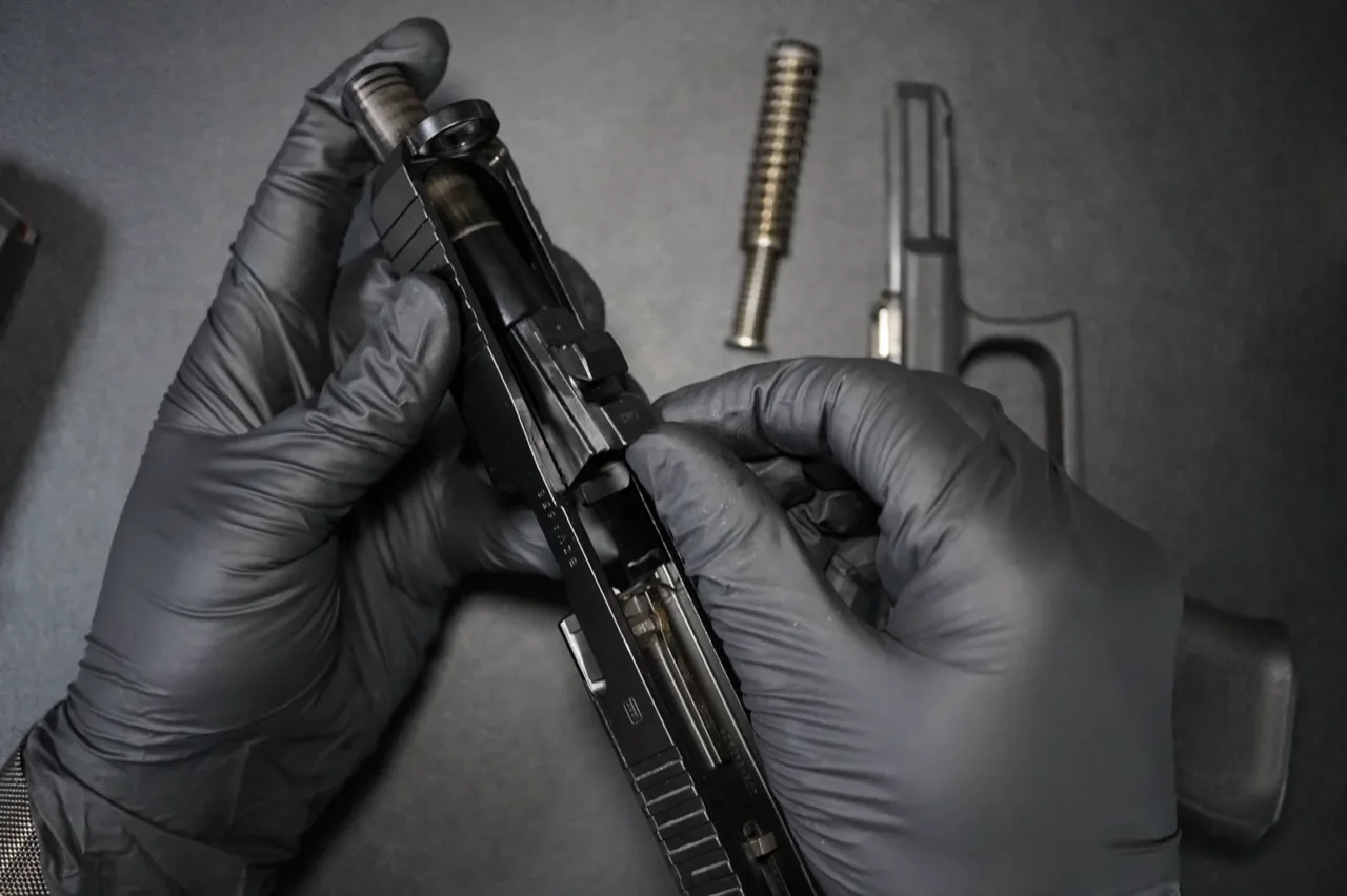 Gloved hands lifting the barrel out of a Glock 19 slide, with the recoil spring and frame on the bench