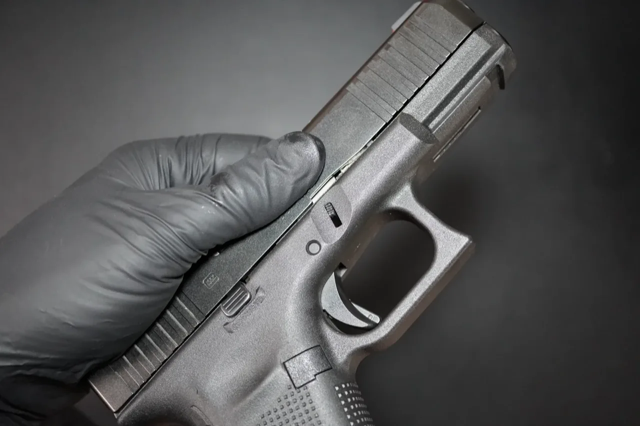 Close-up of a thumb pulling down the Glock 19 slide lock takedown tab
